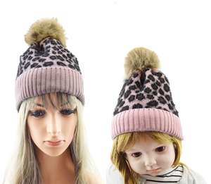 Detail view of matching leopard print knit beanies with pink cuffs and faux fur pom-poms