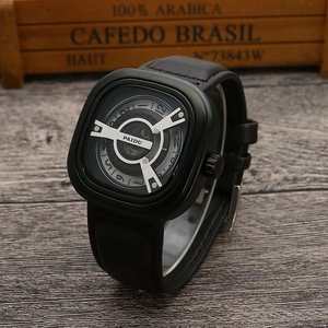 Detail view of square black dial with unique turntable design and leather strap on wood