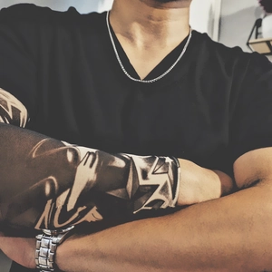 Detail of hip hop keel chain necklace on a model wearing tattoo sleeves and metal watch