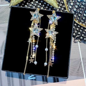 Close-up of golden star-shaped tassel earrings with rhinestones and pearls on a black box