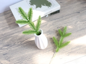 Detailed view of two green artificial pine needles with a ceramic vase on a wooden base