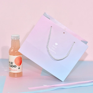 Pink and blue gradient paper gift bag with white rope handles and decorative ribbons