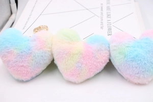 Close-up of three rainbow macabre heart plush keychains with golden rings on white surface