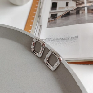 Detail of irregular hammer-textured silver stud earrings hanging on a gray cement tray
