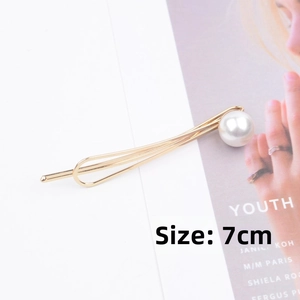 Detail view of a 7cm golden metal hair clip with a round white pearl on the end