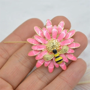 Detailed view of an enamel pink flower brooch with a golden bee on a hand