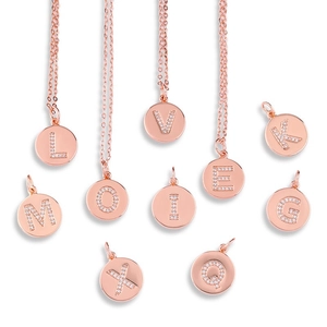 Close-up of rose gold letter pendants with white zircon micro-inlay on white background