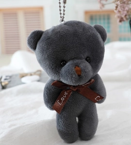 Close-up of small grey plush teddy bear keychain with Love ribbon in a cozy bedroom