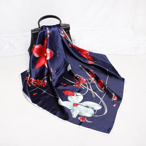 Close-up of luxury silk scarf with red berry and floral print draped on a handbag
