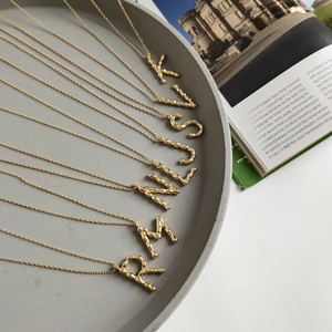 Detail of gold letter necklaces with hammered texture on a dark grey plate