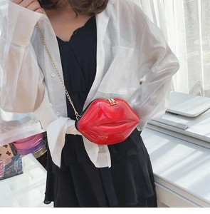 Detailed view of glossy red lip-shaped crossbody bag with gold chain strap worn by model