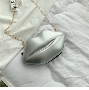 Detail of silver lip-shaped clutch bag with golden metal chain on white fabric