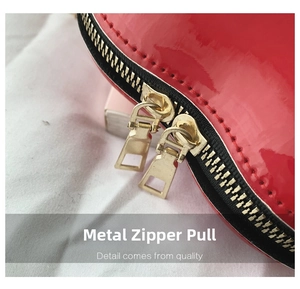 Close-up of bright red patent leather handbag featuring dual golden metal zippers