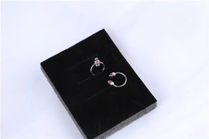 Detail of surgical steel skull nipple rings with red stone eyes on black jewelry tray