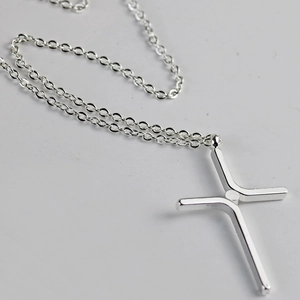 Macro detail of silver cross pendant necklace with a minimalist polished metal finish