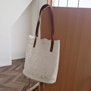 Detail of white floral lace tote bag with dark brown leather handle on wooden chair