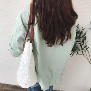 Detailed shot of white floral lace shoulder bag with brown leather strap on model