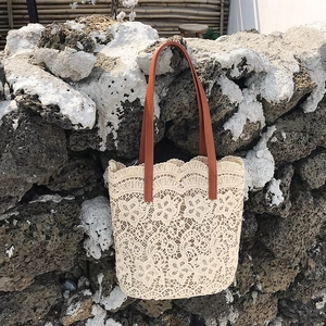 Close-up of beige floral lace tote bag with brown leather handles against stone wall