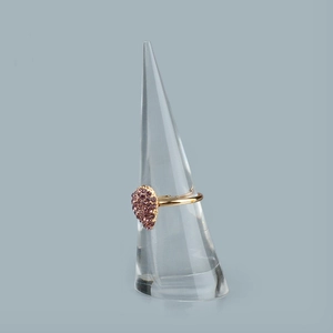 Dettaglio di un anello dorato con strass viola su un supporto in acrilico conico