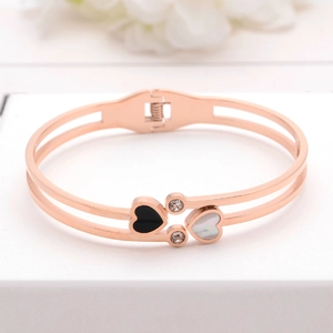 Rose gold heart bangle with black and white heart charms on white geometric display stand