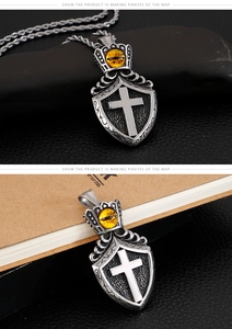 Gothic shield pendant with cross and yellow cat-eye stone shown on black rocks