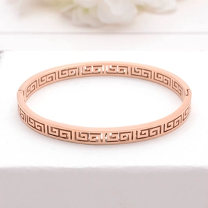 Rose gold stainless steel bangle with Greek key hollow pattern on a white pedestal