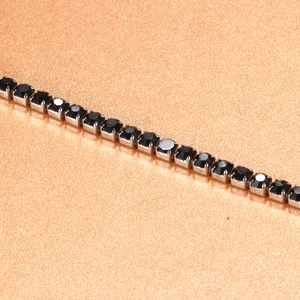 Macro detail of silver tennis chain featuring claw-set black cubic zirconia stones