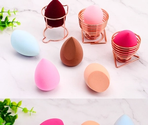 Rose gold geometric stands holding colorful makeup sponges on marble surface