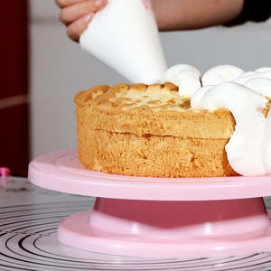 Close-up of icing a round cake with cream on a pink rotating cake turntable stand