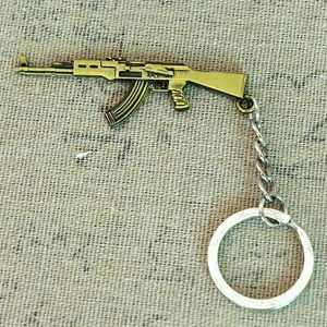 Detail view of a bronze-finished metal AK-47 rifle replica keychain on a burlap surface