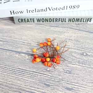 Artificial 8mm orange-red berries on a light wood background for DIY home decoration