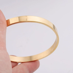 Polished 6mm golden stainless steel C-shaped cuff bracelet held by a hand on grey background