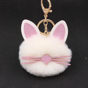 Macro shot of white plush bunny keychain with pink glitter ears and gold clasp on black