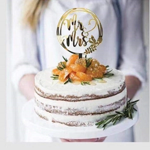Close-up of golden acrylic Mr & Mrs cake topper on cake decorated with rosemary and fruit