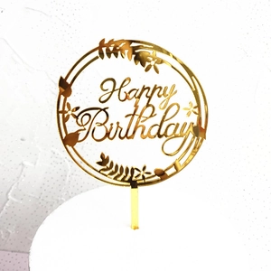 Close-up of a round golden mirror acrylic cake topper featuring a Happy Birthday cutout