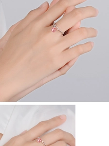 Detail of silver heart-shaped band ring featuring a dangling pink round gemstone charm