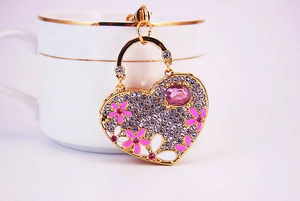 Detail of heart keychain with pink rhinestone flowers on a white porcelain cup
