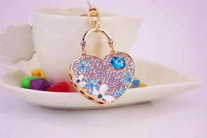 Macro detail of heart-shaped keychain with rhinestones, enamel flowers and blue stone