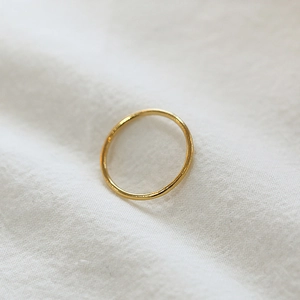 Minimalist slim gold ring shown on a textured white fabric background with soft lighting