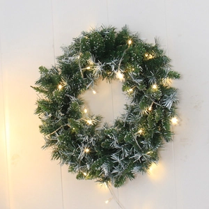 Green Christmas wreath with warm LED lights and silver snow accents on a wood wall