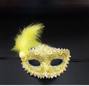 Detail of a yellow Venetian lace mask featuring feathers, sequins, and gold trim decor