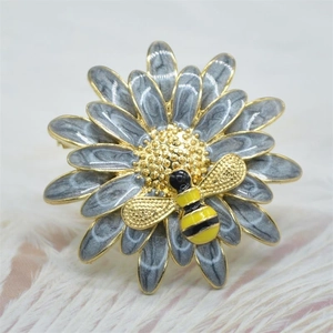 Detailed close-up of a grey enamel flower brooch with a golden bee on a plush background