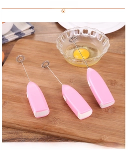 Pink handheld electric milk frother and coffee mixer placed on a rustic wooden board