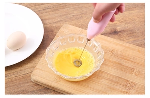Action shot of pink handheld electric milk frother whisking eggs in a glass bowl