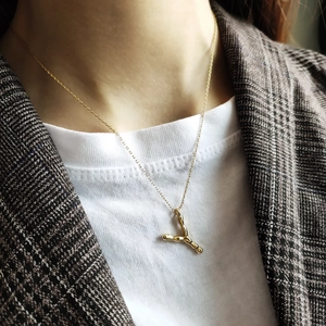Detailed view of an artistic gold Y-letter pendant on a fine chain worn with a blazer