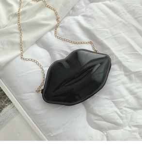 Close-up of black lip-shaped patent leather bag with a fine gold chain on white fabric