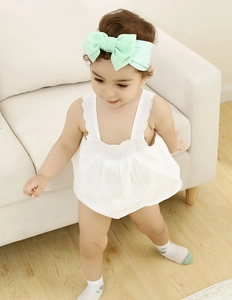 Close-up of a baby wearing a white ruffle romper with a mint green bow headband
