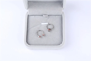 Macro detail of silver medical steel skull body rings with red crystal eyes on grey velvet
