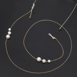 Elegant gold metal glasses chain with white pearl accents on a textured black background