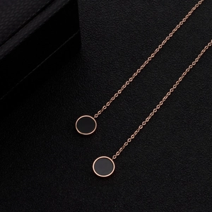 Dettaglio di orecchini a catena lunga oro rosa con ciondoli neri tondi eleganti